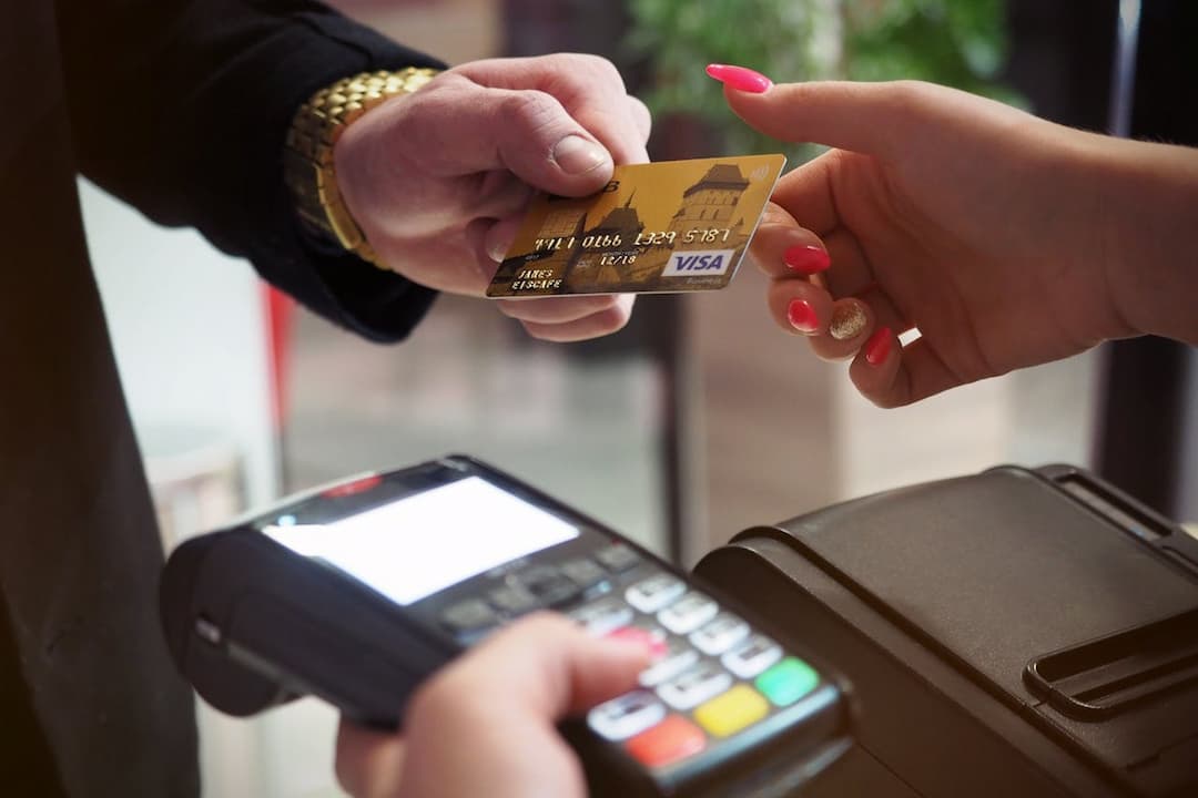 Close-up of a credit card handover during a transaction, gold Visa card being passed from one person to another, payment terminal in foreground