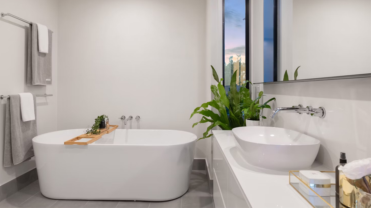 Modern white bathroom, freestanding bathtub with wooden tray, vessel sink, large mirror, indoor plant by tall window