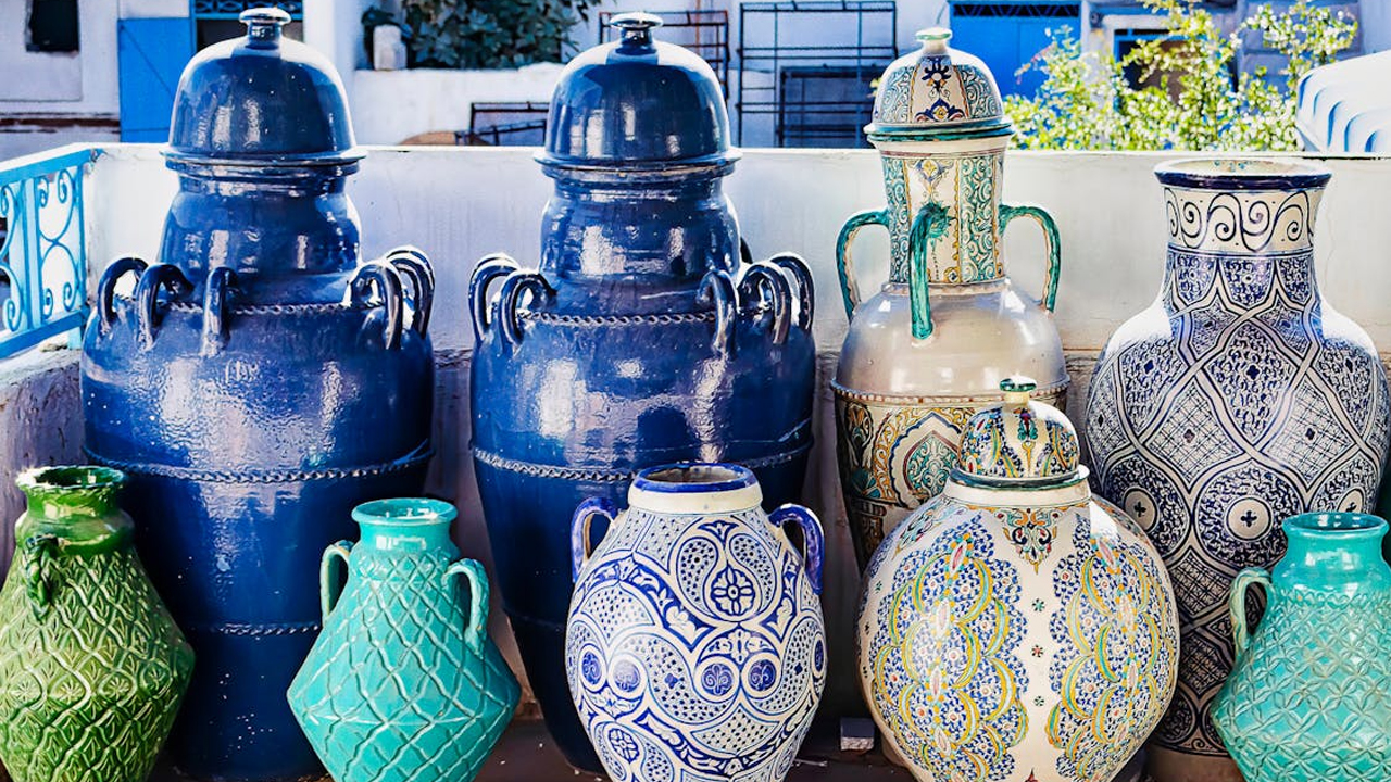 Vintage ceramic vases, brown and black finishes, hand-painted floral patterns, displayed on a wooden wall-mounted shelf with lace-edged linens, warm ambient lighting