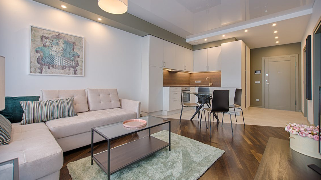 Modern living room and kitchen area, beige sectional sofa, black coffee table, dining set, recessed ceiling lights, and wood flooring