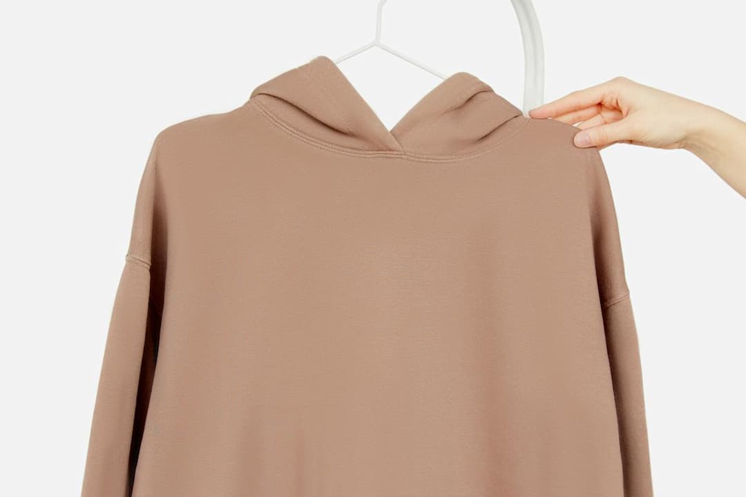 Brown hoodie on a white hanger, back view, minimal design, hand holding hanger, plain white background