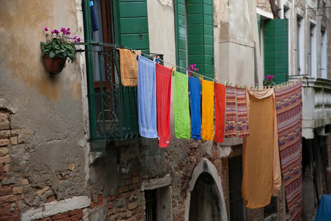 Colorful towels and fabrics hanging on a clothesline between old buildings with green shutters