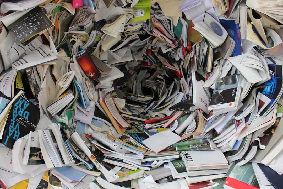 A chaotic spiral pile of open books and papers forming a vortex-like structure, with pages jutting out in all directions