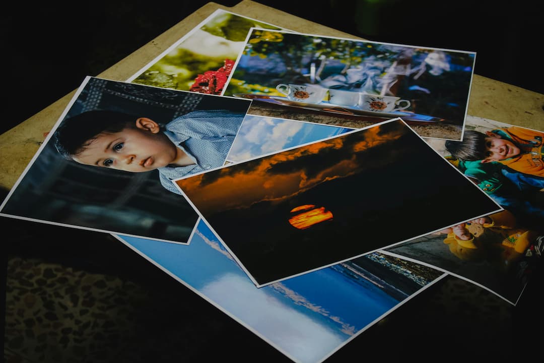 Several printed photographs spread out on a table, including images of a young child, a sunset, tea cups, beach scenes, and playful moments