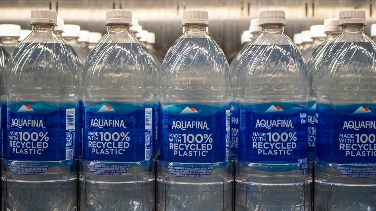 stacked clear plastic water bottles, blue caps, wrapped in thin blue netting, compacted for recycling