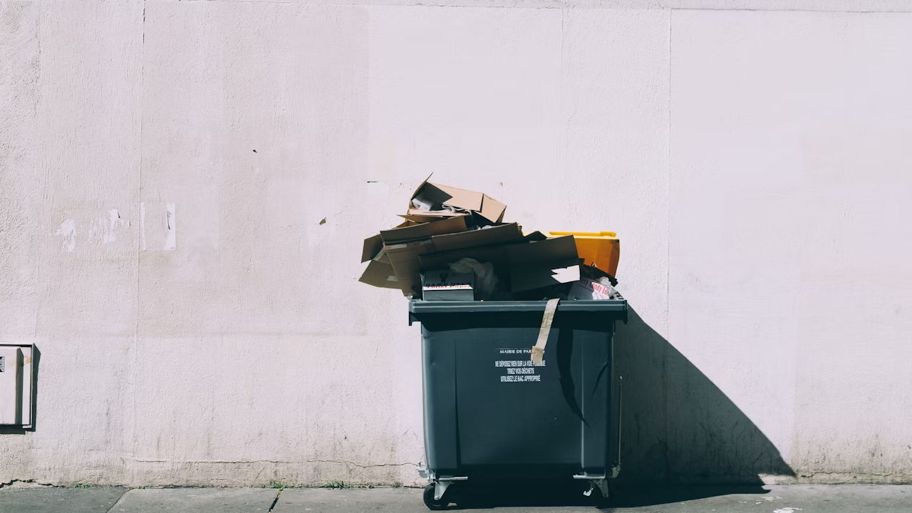 trash bin, foot pedal at the base, slightly open lid, plastic liner inside, placed against a tiled wall, clean exterior surface