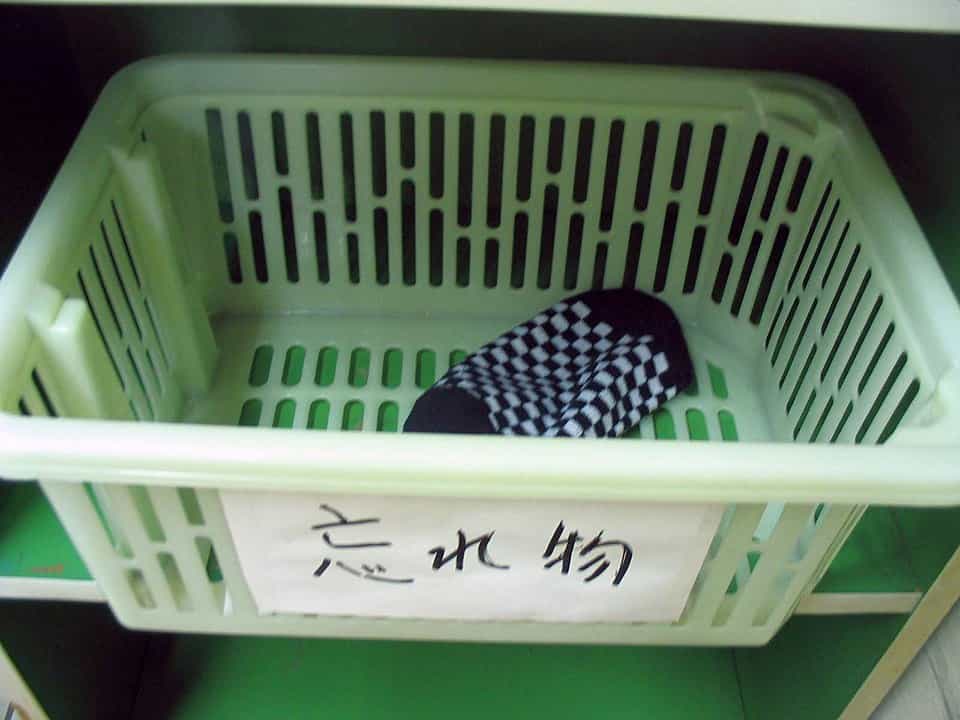 A single black-and-white checkered sock placed inside a light green plastic basket labeled with Japanese character