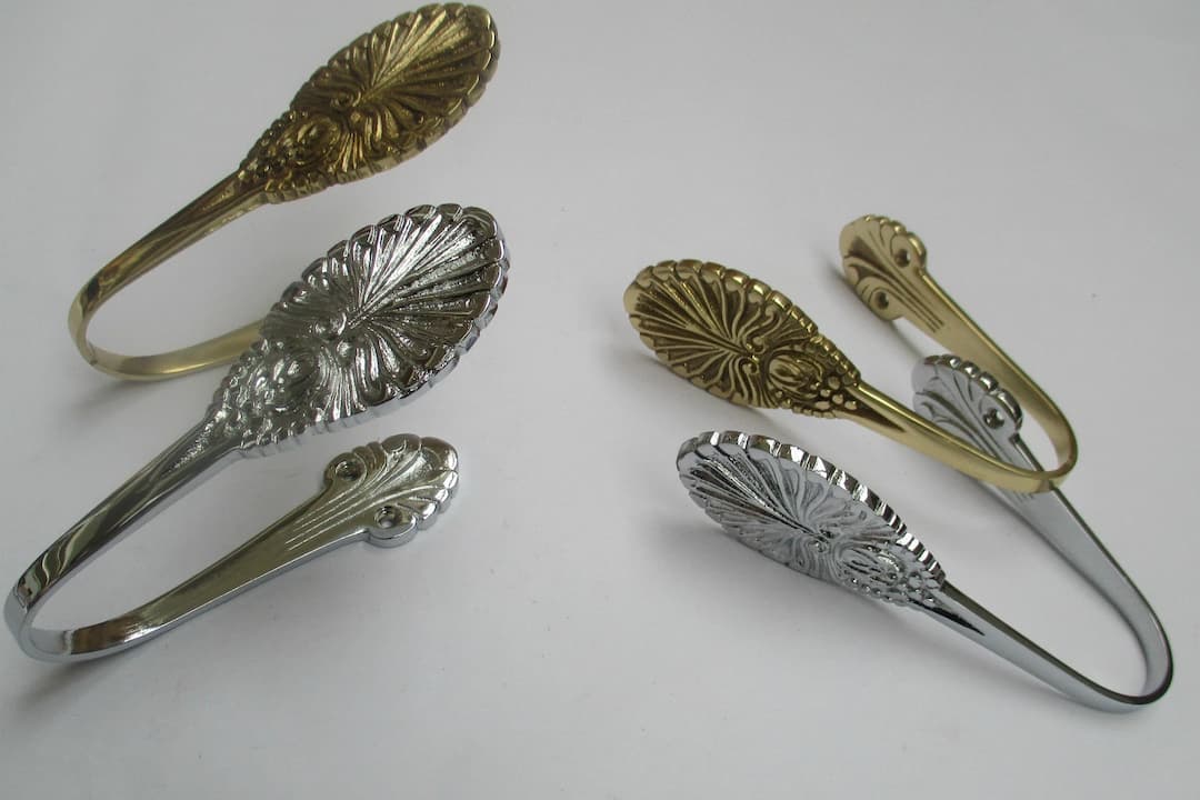 ornate metal curtain tiebacks, two gold and two silver, vintage floral design, displayed on white background