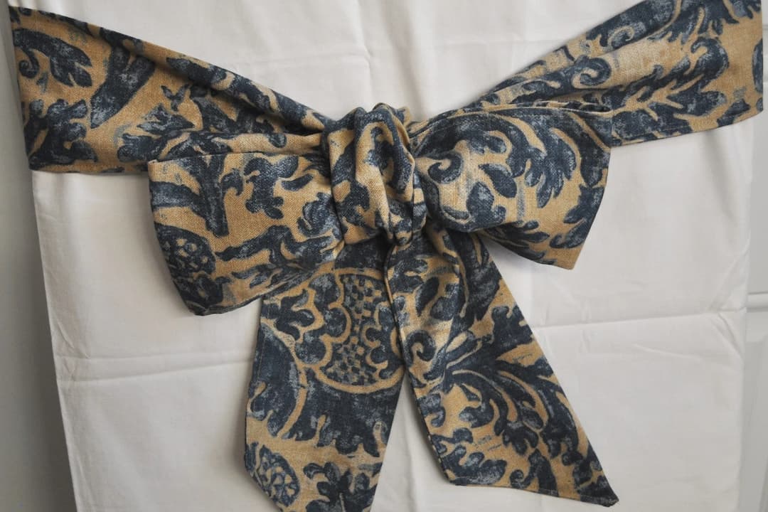 decorative fabric bow in navy and gold damask pattern, tied around white curtain or chair cover