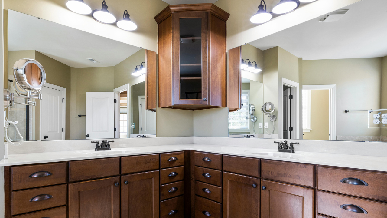 Corner bathroom vanity with dual sinks, dark wooden cabinets, large wall mirrors, and multiple overhead lights