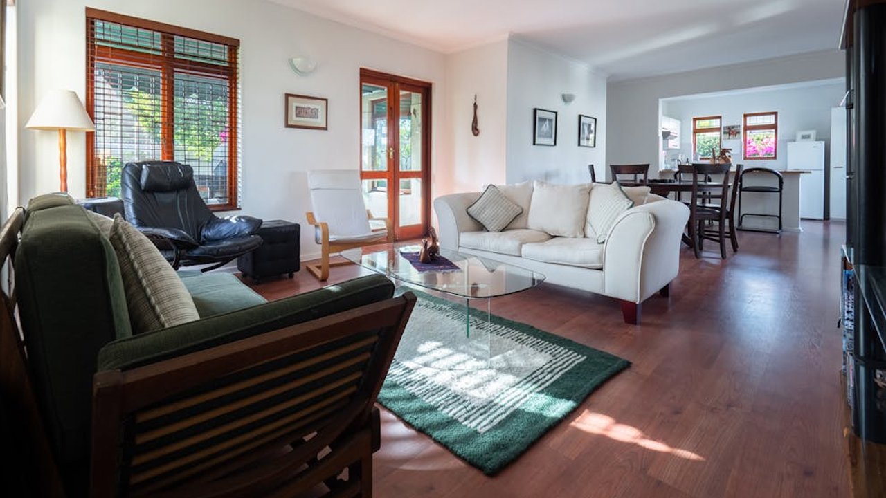 Spacious living room, cream and dark green sofas, black recliner, glass coffee table, wooden flooring, green rug