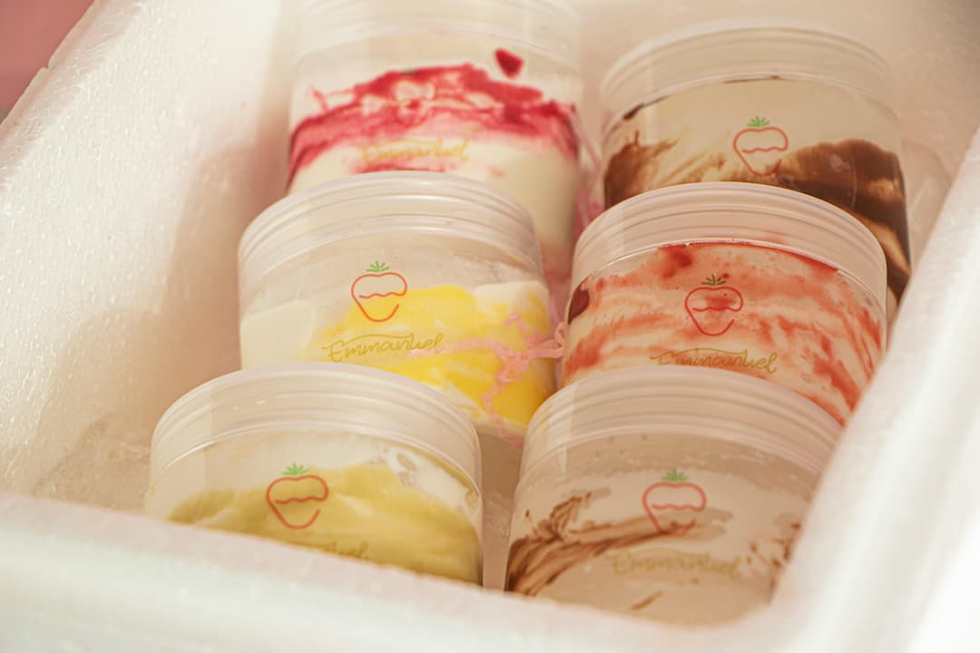 Six plastic tubs of Emmanuel-branded swirled ice cream in assorted flavors, placed in a white foam cooler