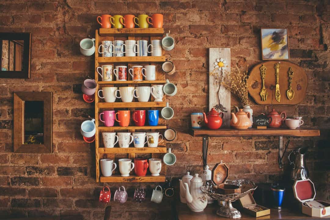 brick wall kitchen, wooden mug rack with assorted colorful mugs, wooden shelf with teapots and cups, vintage utensils on display, decorative frames, cozy rustic setup