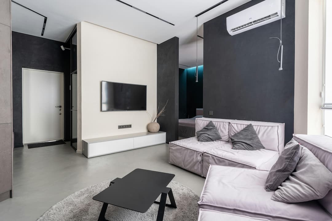 Modern minimalist living room, white and charcoal walls, wall-mounted TV, sleek black coffee table, light gray sectional sofas with gray throw pillows