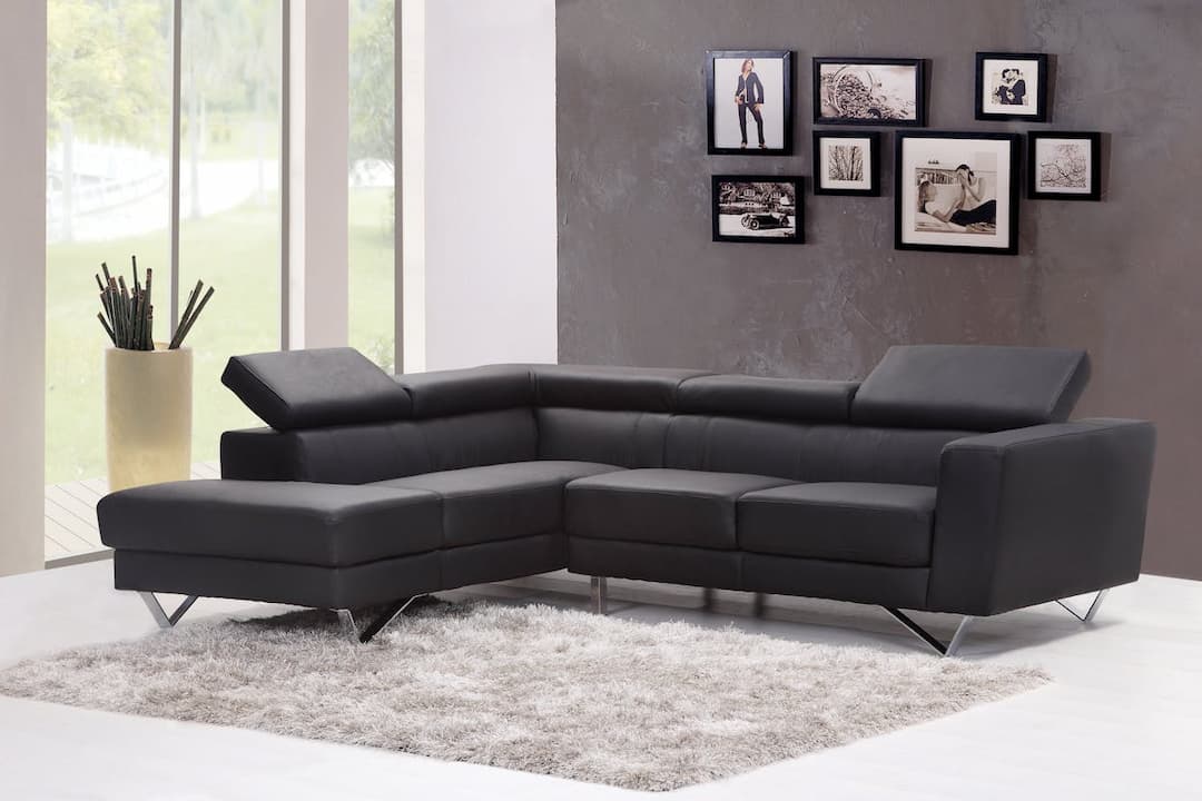 black L-shaped sectional sofa, adjustable headrests, silver metal legs, soft gray shag rug, gray textured wall, photo frame collage, large windows, beige floor vase with decorative sticks