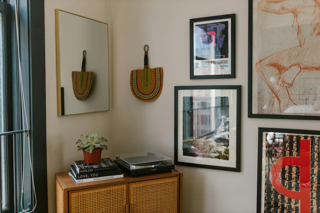 A thoughtfully decorated home corner, perfect for relaxation or listening to vinyl records. The mix of framed artwork, natural textures, and personal touches like the fan and succulent suggest a creative and curated living space
