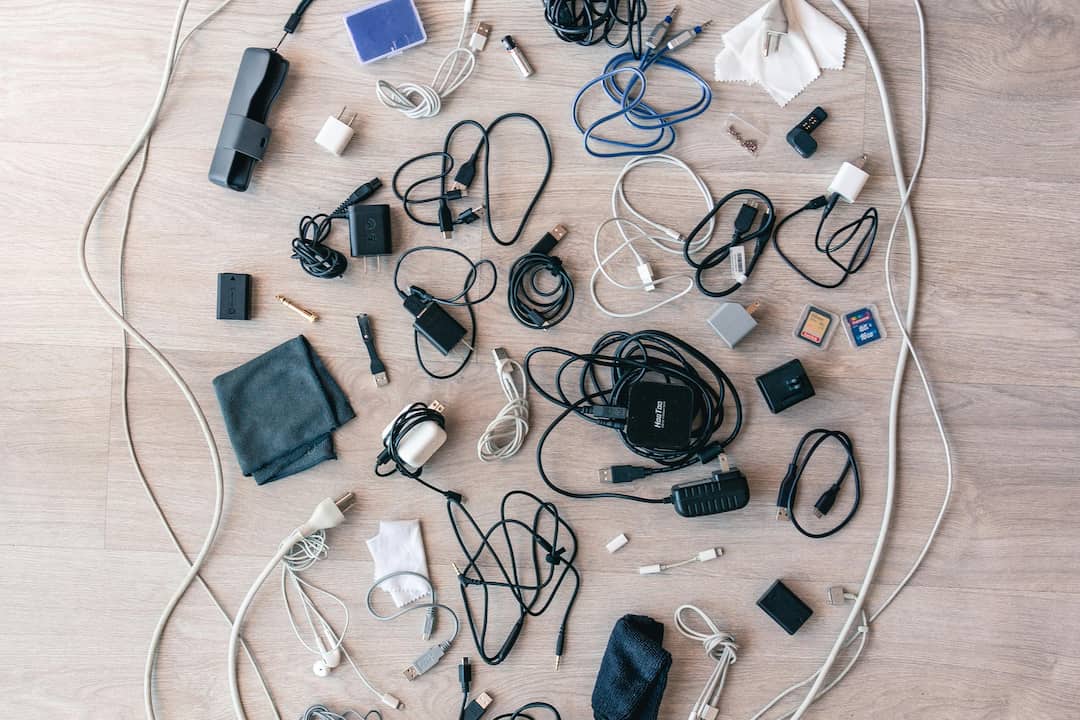 Assorted electronic accessories and tangled charging cables spread across a wooden floor, including adapters, memory cards, earphones, and plugs