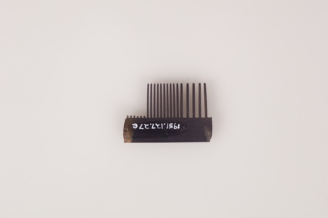 A small black broken comb with uneven teeth, featuring white alphanumeric markings on the base