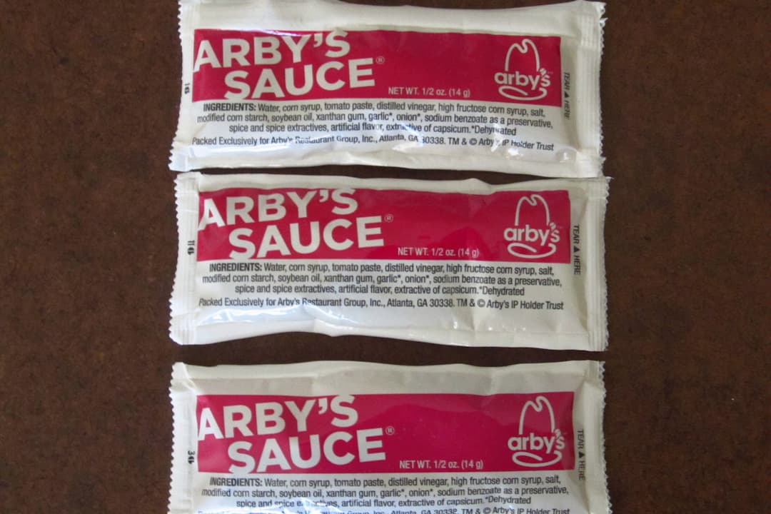 Three Arby’s Sauce packets arranged vertically on a brown surface