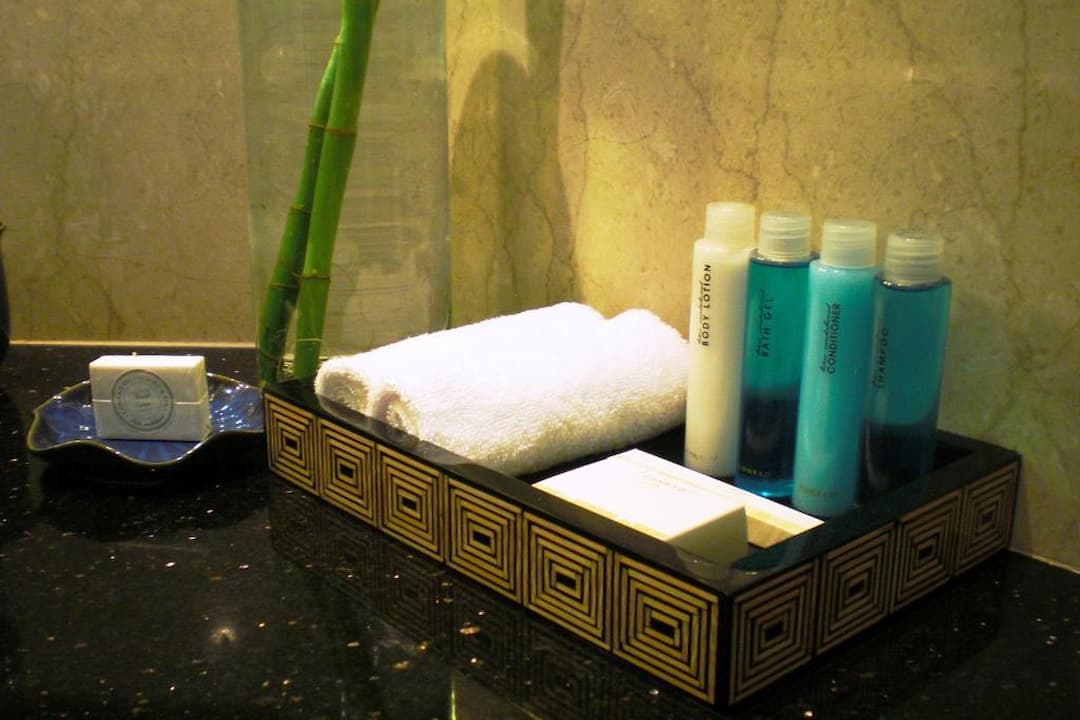 bathroom countertop with a decorative tray containing white rolled towel, bottles of shampoo, conditioner, shower gel, and body lotion, bar soaps, blue soap dish with round soap, bamboo stalk in a glass vase