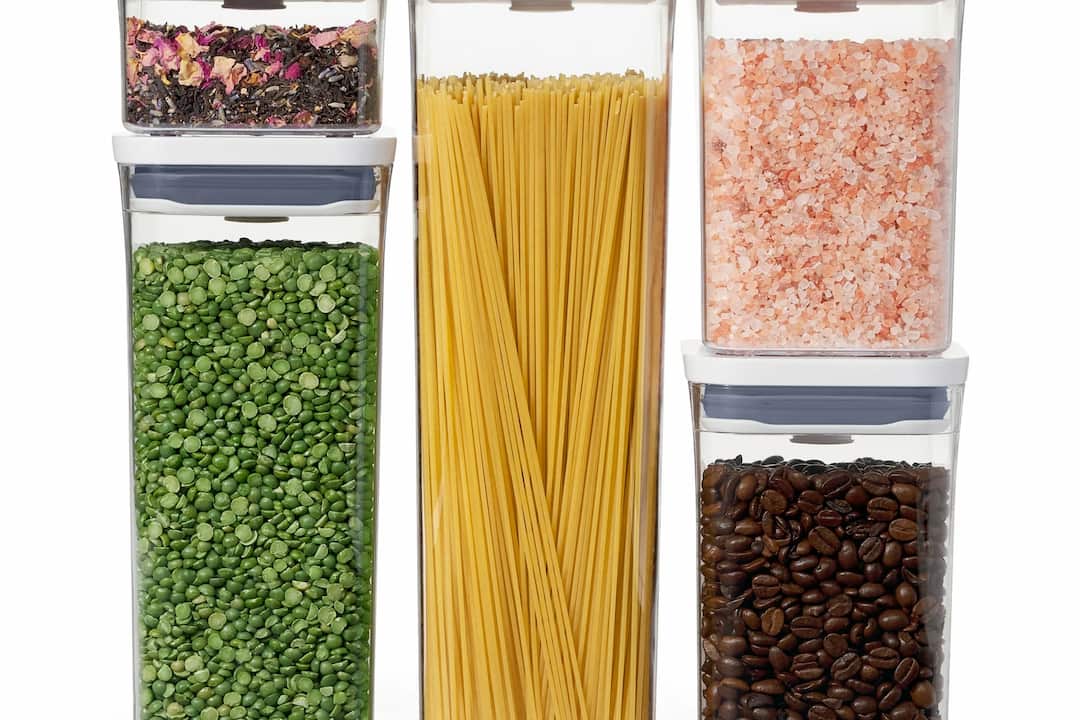 Five clear airtight containers filled with dried rose tea, green split peas, uncooked spaghetti, pink Himalayan salt, and coffee beans