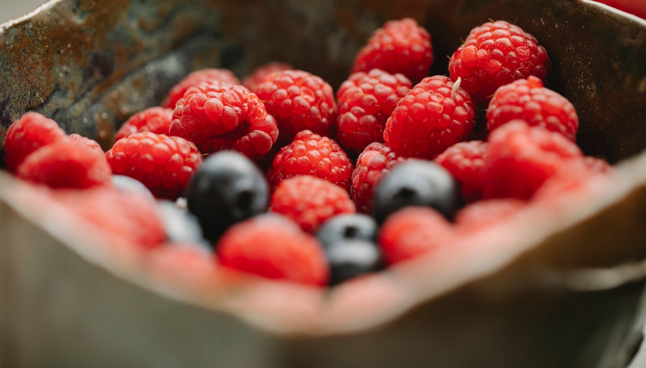 Close-up of fresh raspberries and blueberries in a rustic metal container