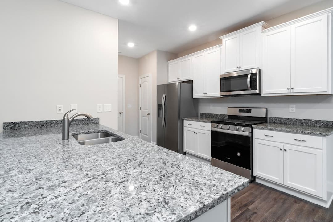 Modern kitchen with granite countertops, stainless steel double sink, white cabinets, stainless steel fridge, microwave, and gas oven, hardwood floors, bright lighting