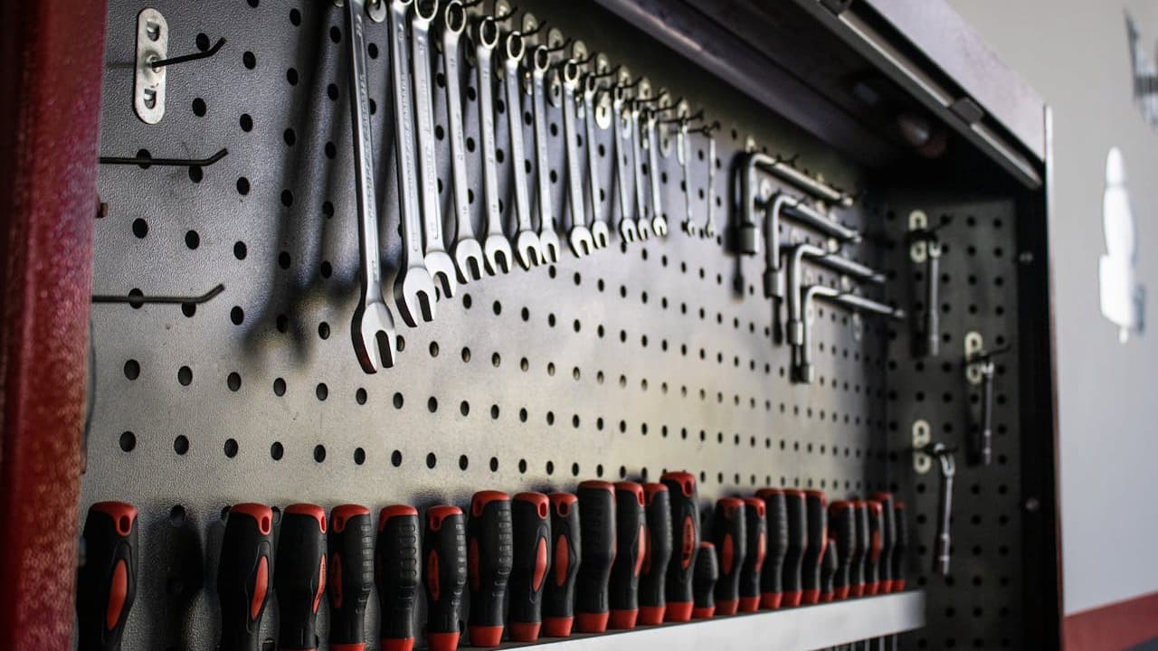 Neatly organized hand tools on a perforated wall panel, including wrenches, screwdrivers with red and black handles, and hex keys, all arranged by size inside a tool cabinet