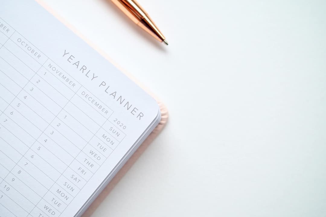 Close-up of a yearly planner and a rose gold pen on a white surface
