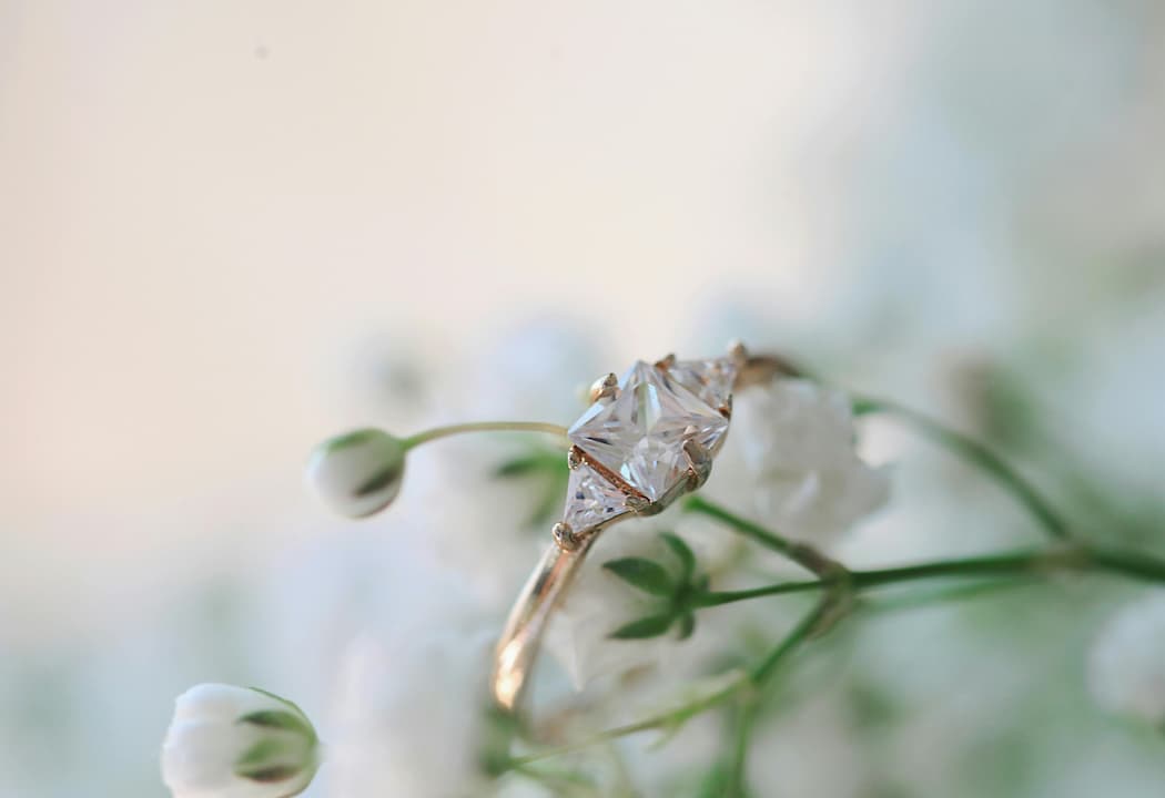 Gold ring with a princess-cut diamond center stone and two triangular side stones, placed on white baby’s breath flowers
