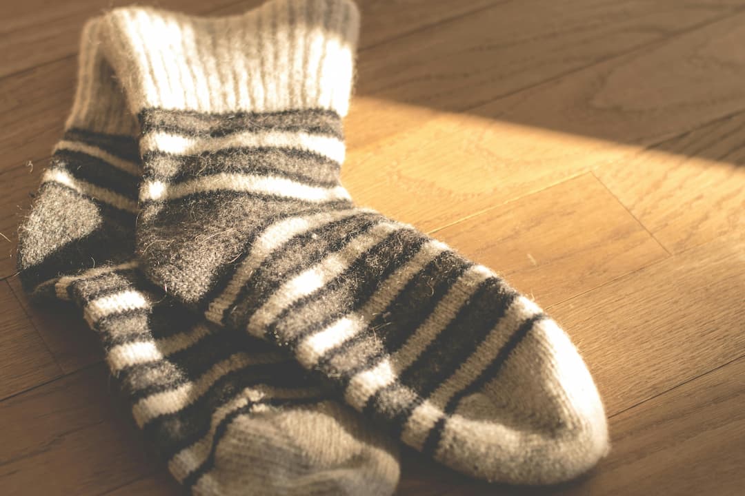 A pair of woolen, striped black-and-white socks lying on a wooden floor, partially illuminated by warm sunlight