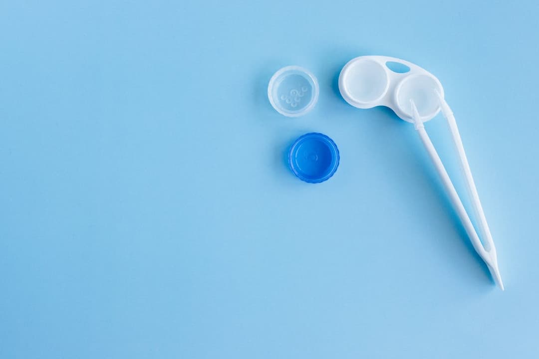 Contact lens case with open caps and white applicator on light blue background
