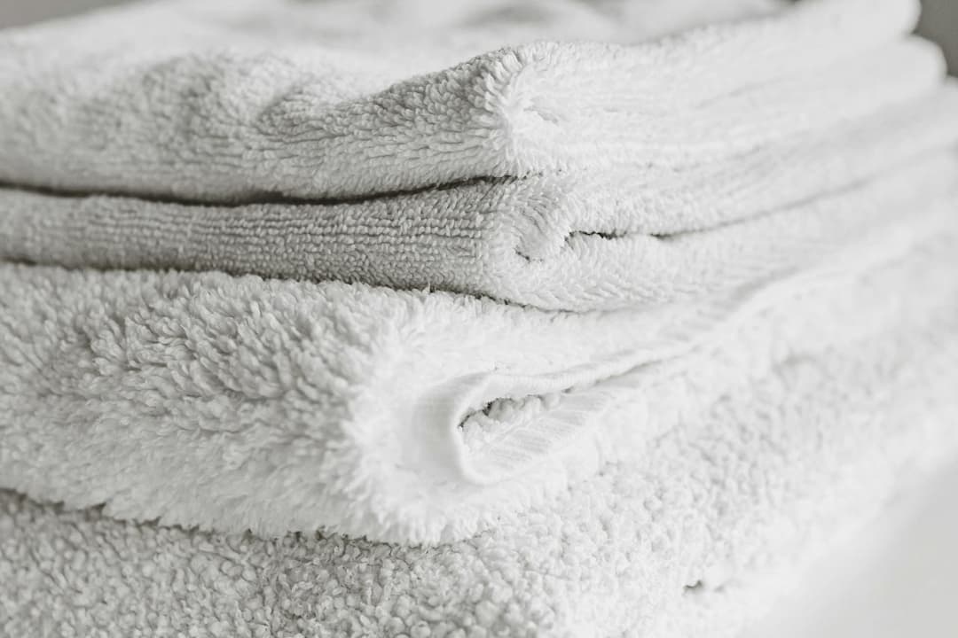 Stack of neatly folded white towels on a flat surface, showing soft, fluffy texture and clean fabric layers