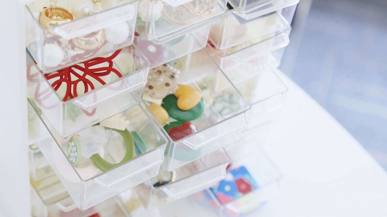 Clear plastic drawer organizer, filled with small colorful toys and trinkets, various compartments holding different items, white tabletop surface, bright and tidy storage solution