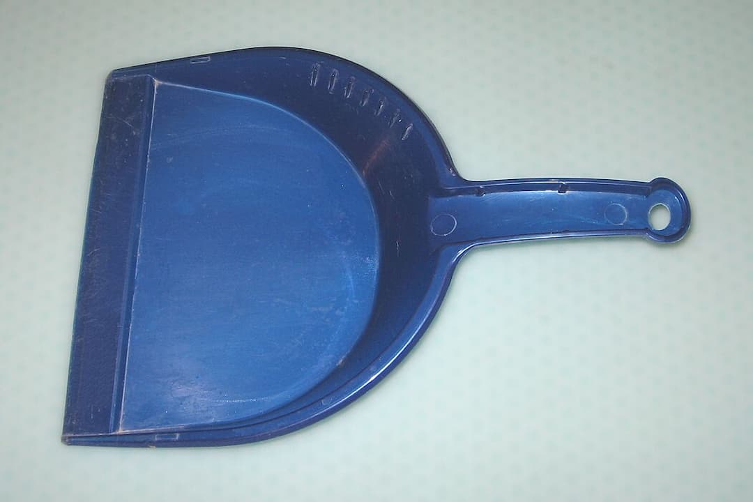Blue plastic dustpan with a flat edge and a handle, placed on a light patterned surface