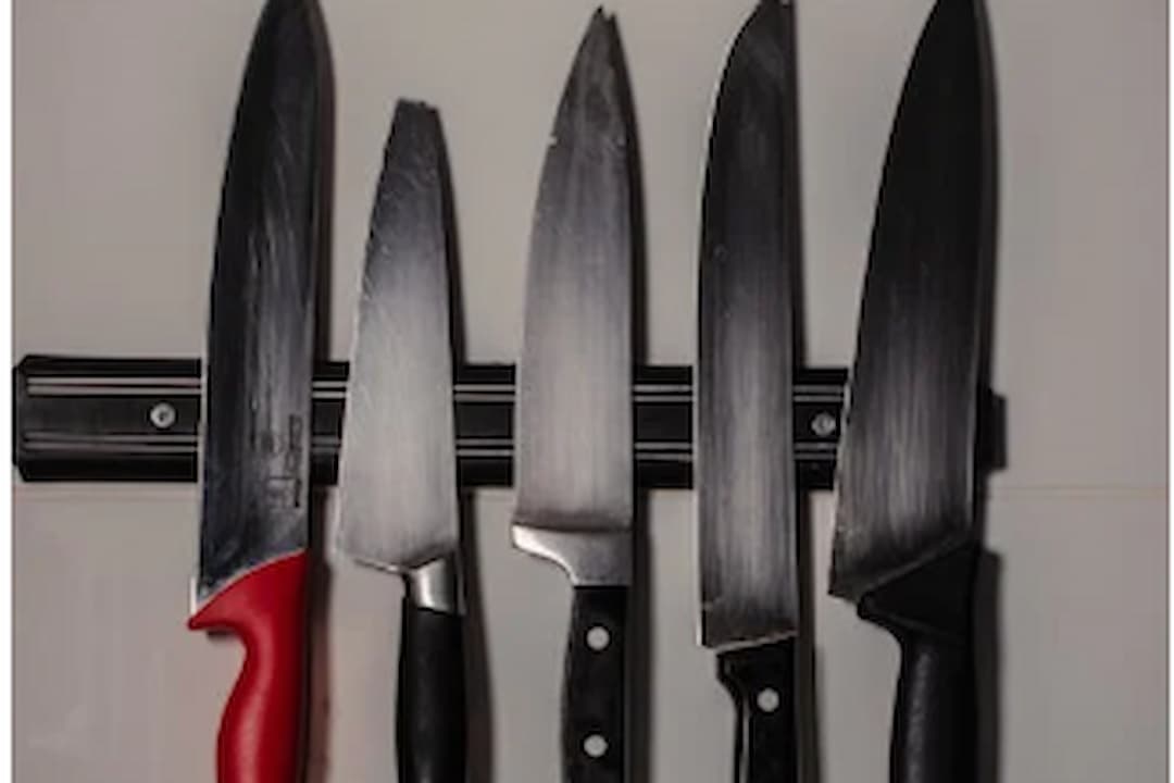 Five kitchen knives with varying handle styles are mounted on a magnetic knife strip attached to a wall