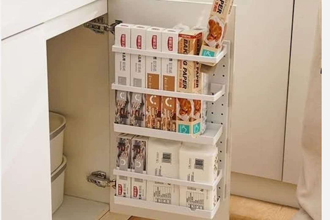 White cabinet door organizer with multiple racks holding baking paper, plastic wrap, and food storage bags, neatly arranged inside a kitchen cupboard