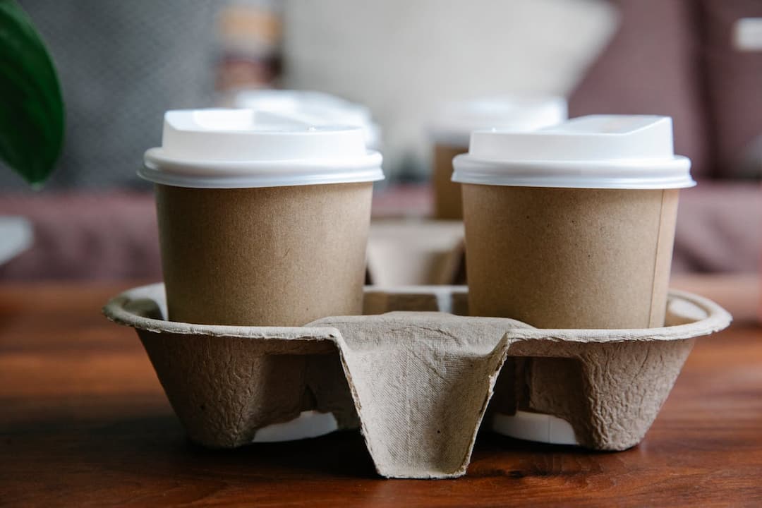 Four disposable coffee cups with white lids in a cardboard holder