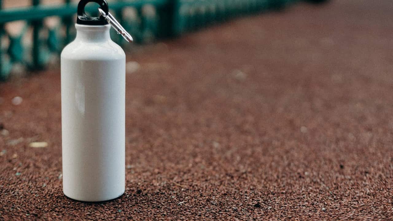 White reusable water bottle with a black cap and carabiner placed on a red rubber running track