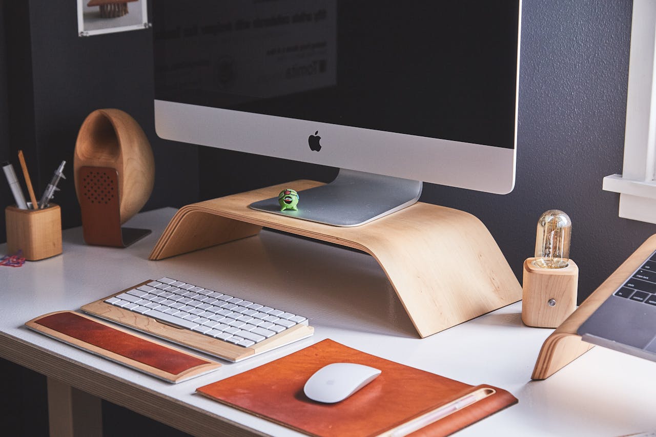 Minimalist workspace with an Apple iMac, wooden accessories, and leather desk pads on a white desk