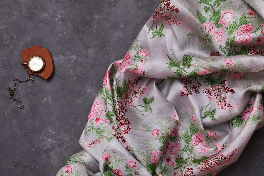 light grey fabric with pink and green floral print, draped on dark textured surface, vintage pocket watch with chain resting on piece of terracotta