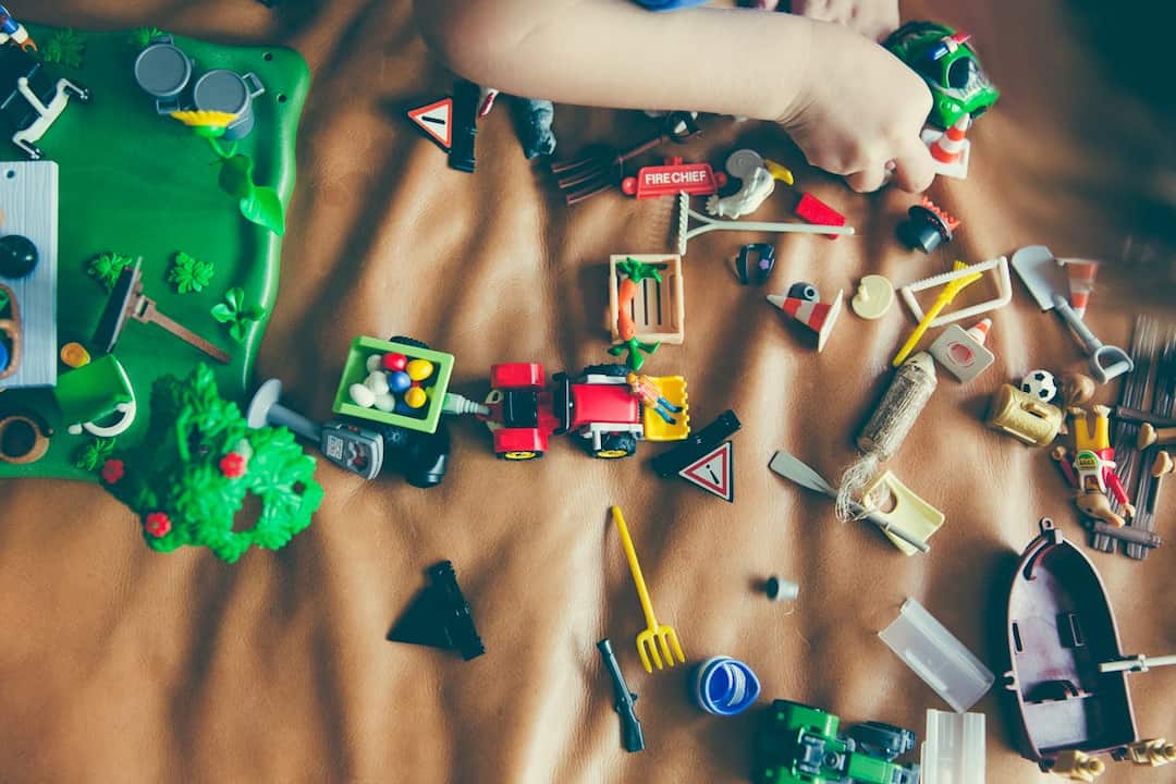 Child playing with colorful plastic toy figures and vehicles on a brown surface