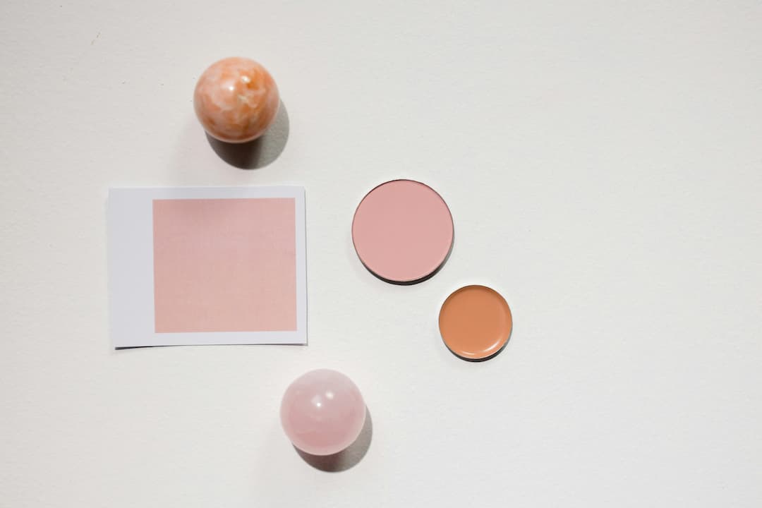 Pink and orange color swatches with two marble spheres, one rose quartz and one orange, arranged on a white surface