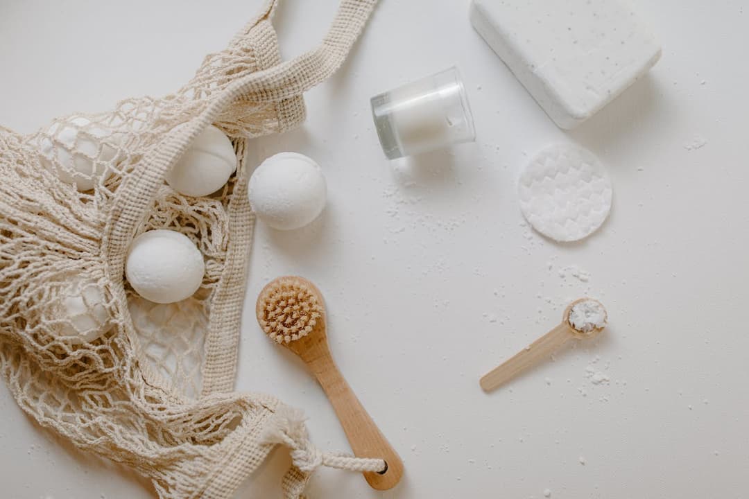 white bath bombs, mesh bag, wooden body brush, bar soap, cotton pads, candle, wooden spoon with powder, white background