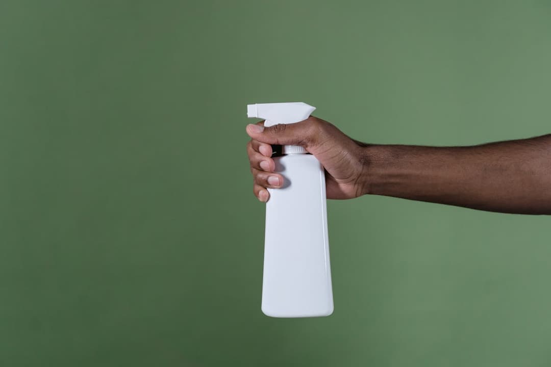 hand holding white spray bottle, green background, angled sideways grip