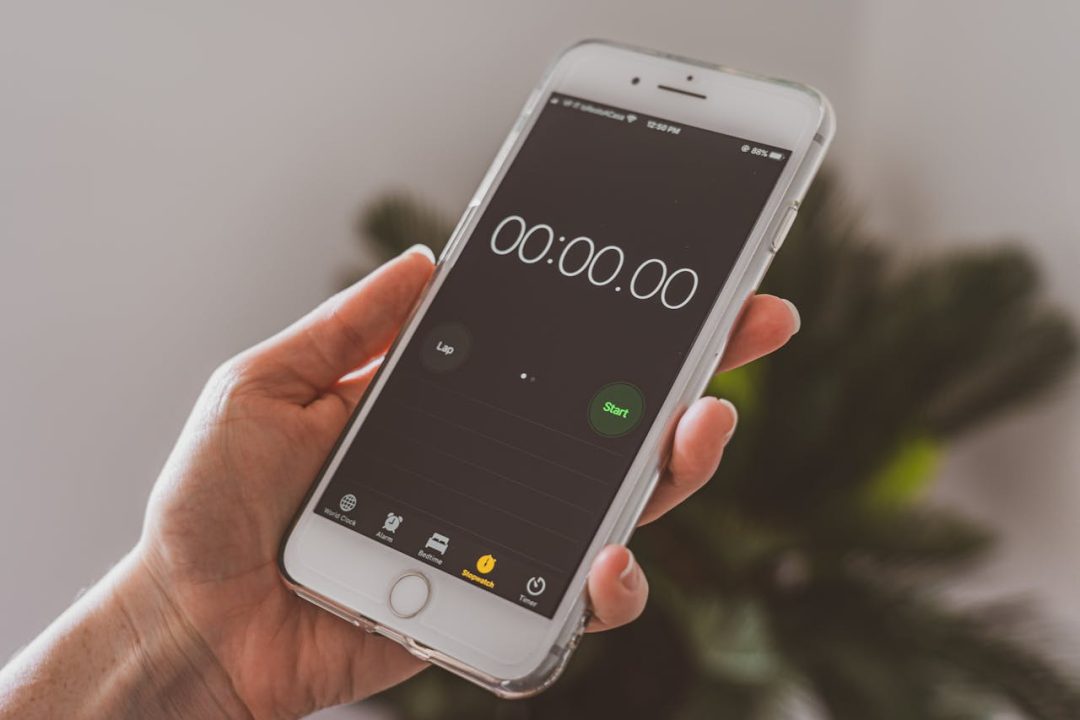 Hand holding a smartphone displaying a stopwatch at 00:00.00 with the start button highlighted